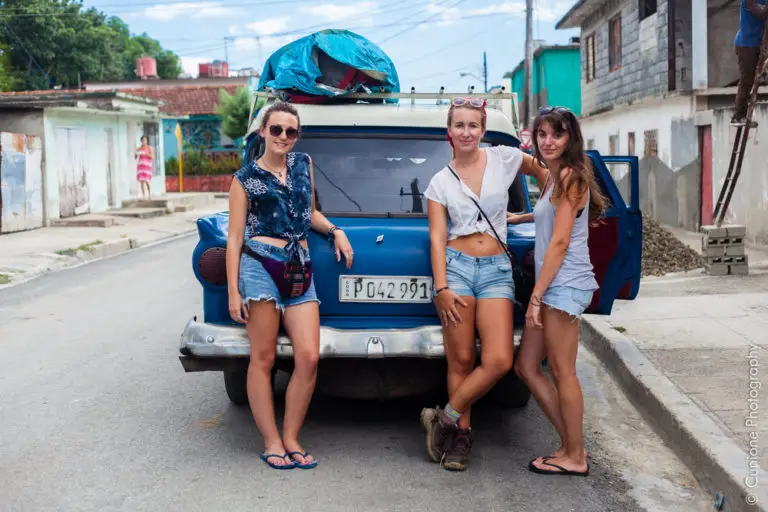 girls posing in front of vintage car in Cuba