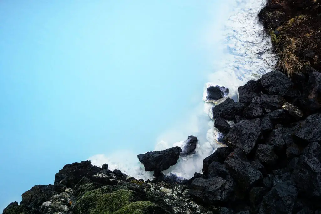 milky blue lagoon water next to black rocks